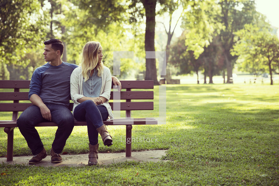 a couple sitting on a park bench looking away from each other 