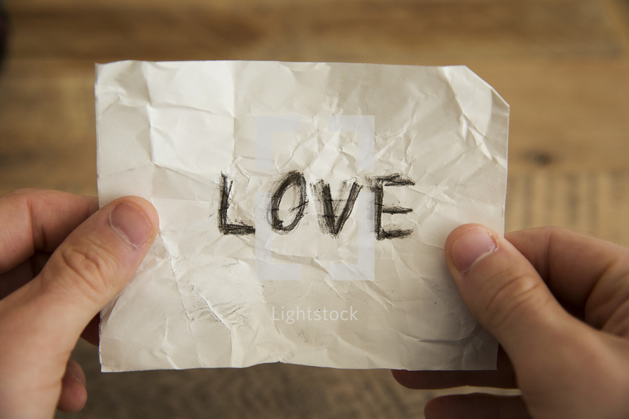 hands holding a piece of crumpled paper with the word love