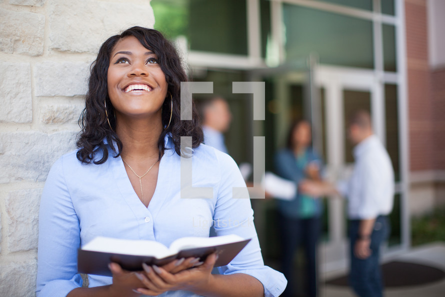 a smiling African American woman holding a Bible looking up to God 