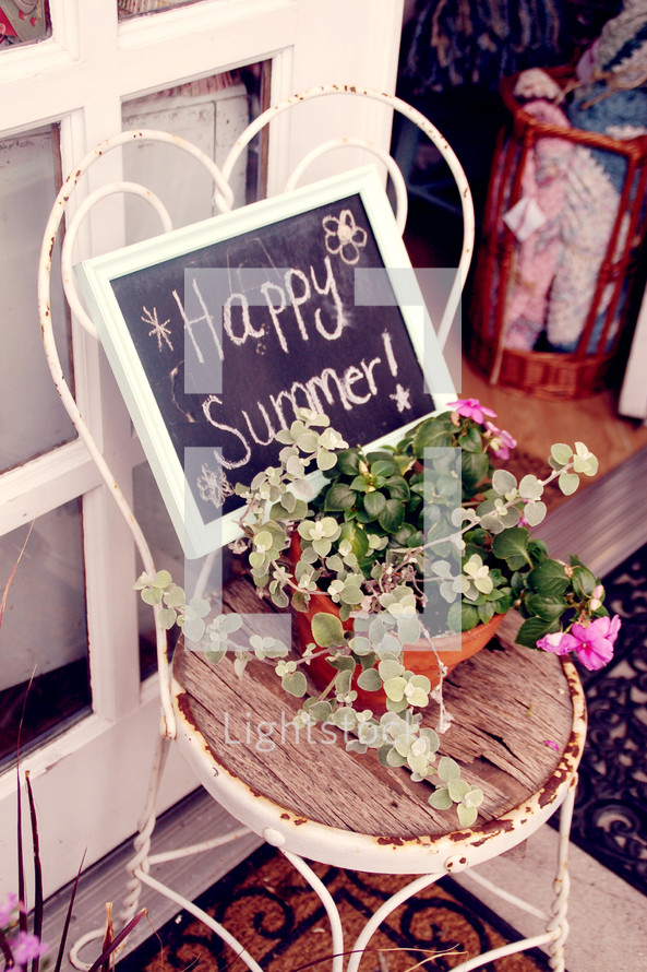 A pot of flowers on an old chair with a sign reading, "Happy Summer!"