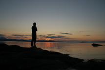 Silhouette of a man standing before a lake at sunset.