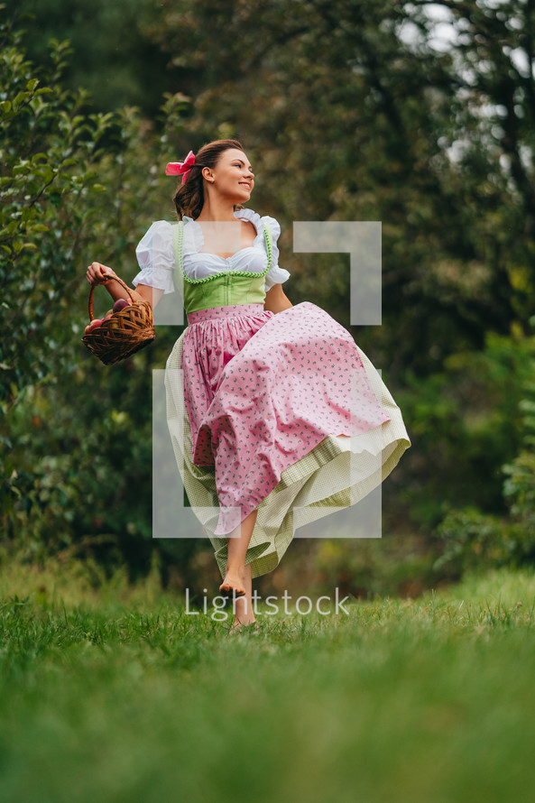 Beautiful woman picking up ripe red apple fruits in green garden. Girl in cute long peasant dress. Organic village lifestyle, agriculture, gardener occupation. High quality