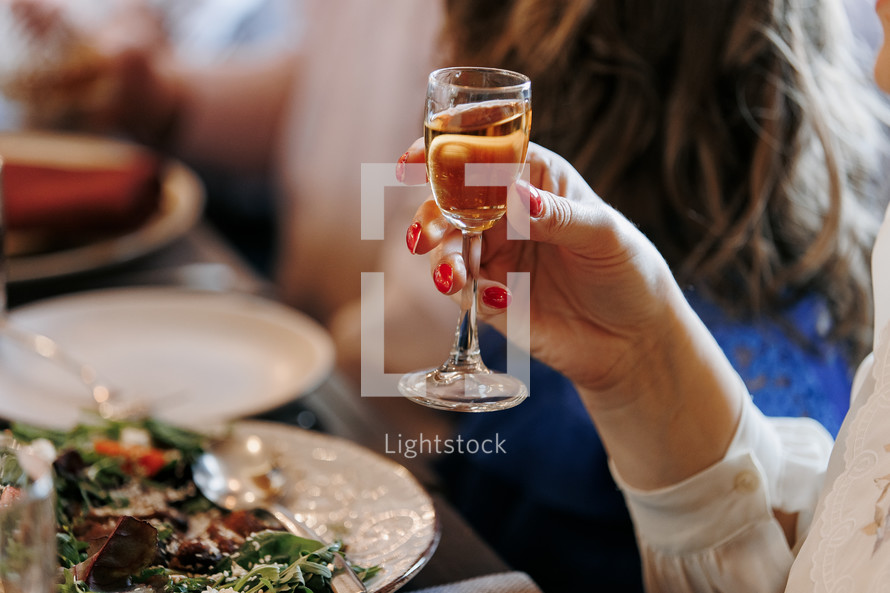 Unrecognisable woman holding glass of alcohol drink, cognac, liquor makes toast by the festive table, fun for a birthday, wedding, anniversary or any other holiday, happy atmosphere, friendly company