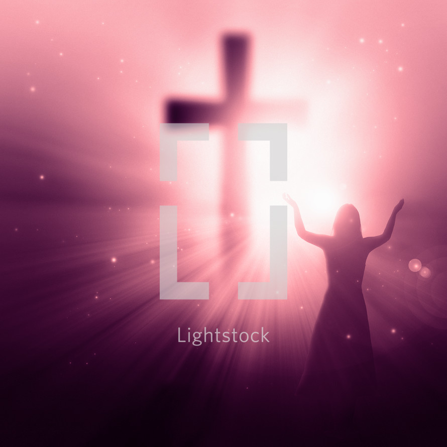 woman standing in front of a glowing cross with her hands raised in worship and praise