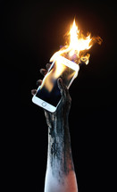a raised tattooed arm holding a burning cellphone 