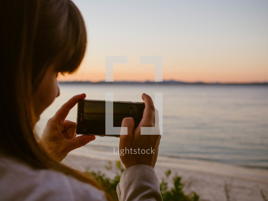 a woman taking pictures of a beach at sunset 