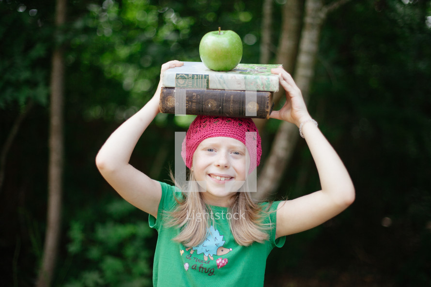 a child holding a stack of books on her head 