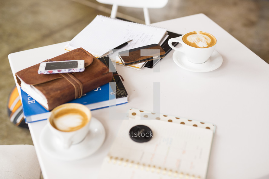 Bible, journal, notebook, coffee cup, cellphone, and pen on a white table 