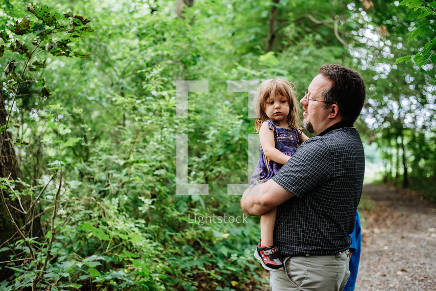 father carrying his daughter on a trail in the woods 
