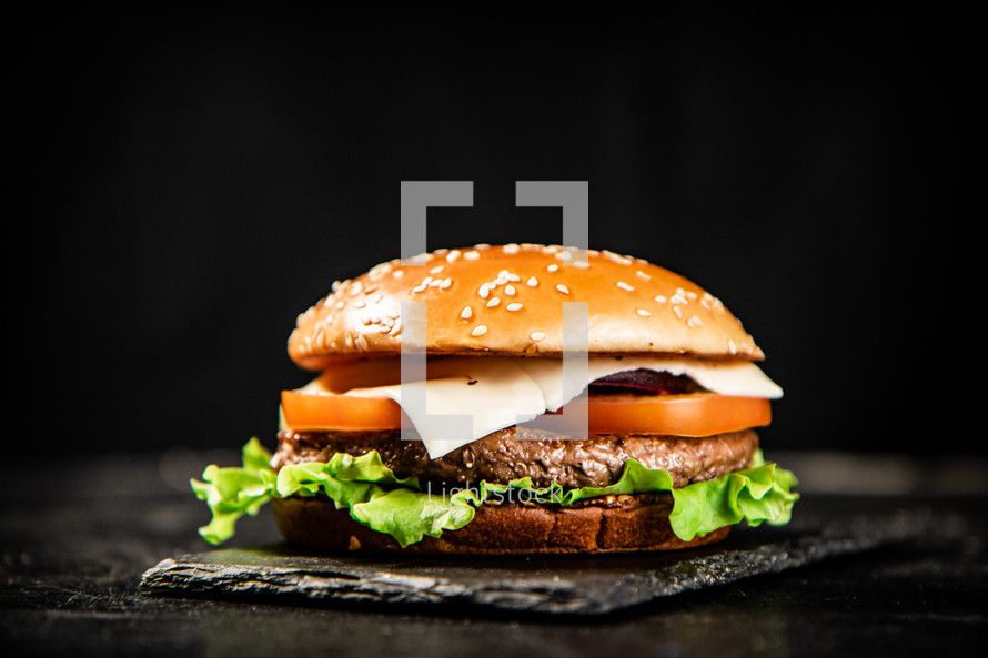 A burger on a stone board on a table. On a black background. High quality photo