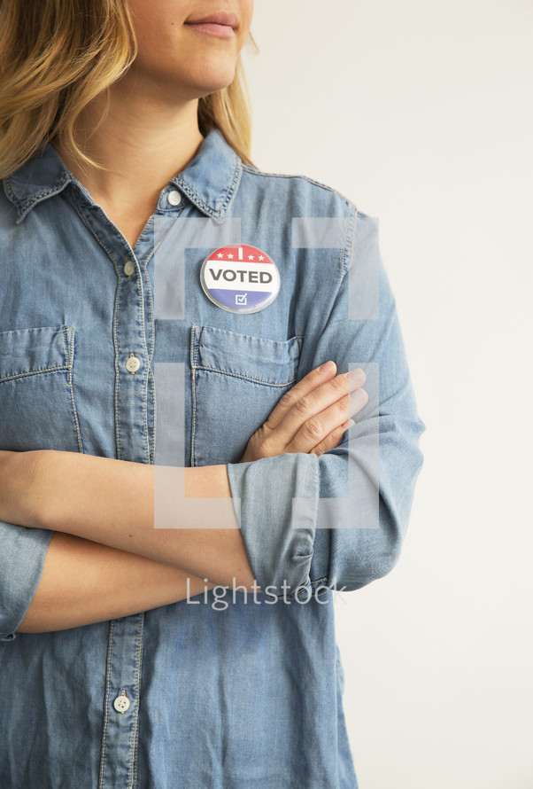 A woman with arms crossed wearing a denim shirt and an ,"I Voted," button.