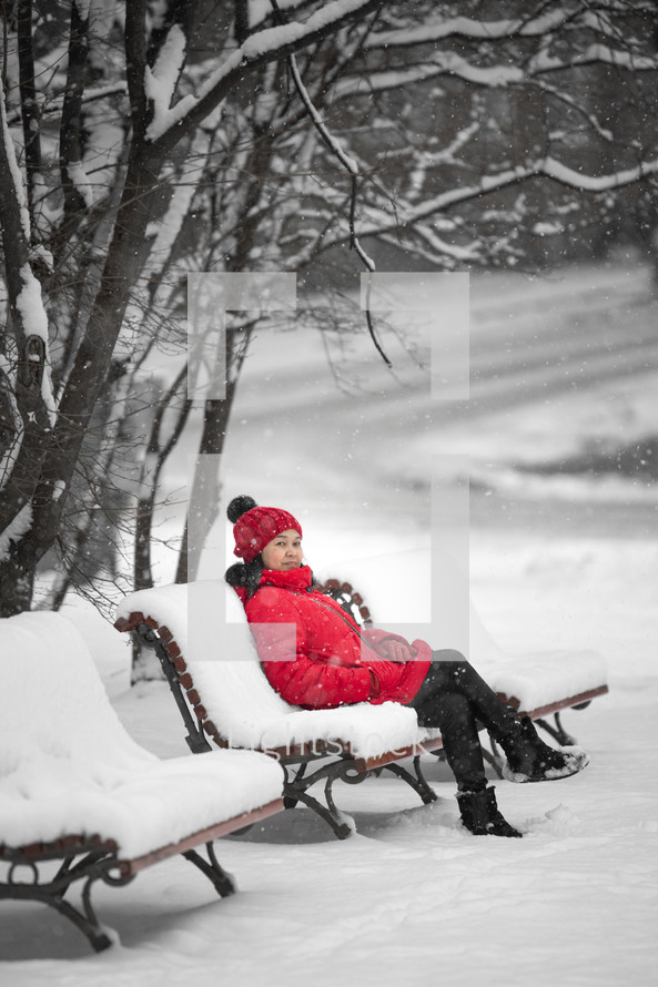 a woman in a red coat sitting on a bench in snow 