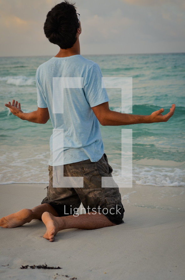 man on his knees in prayer to God on a beach
