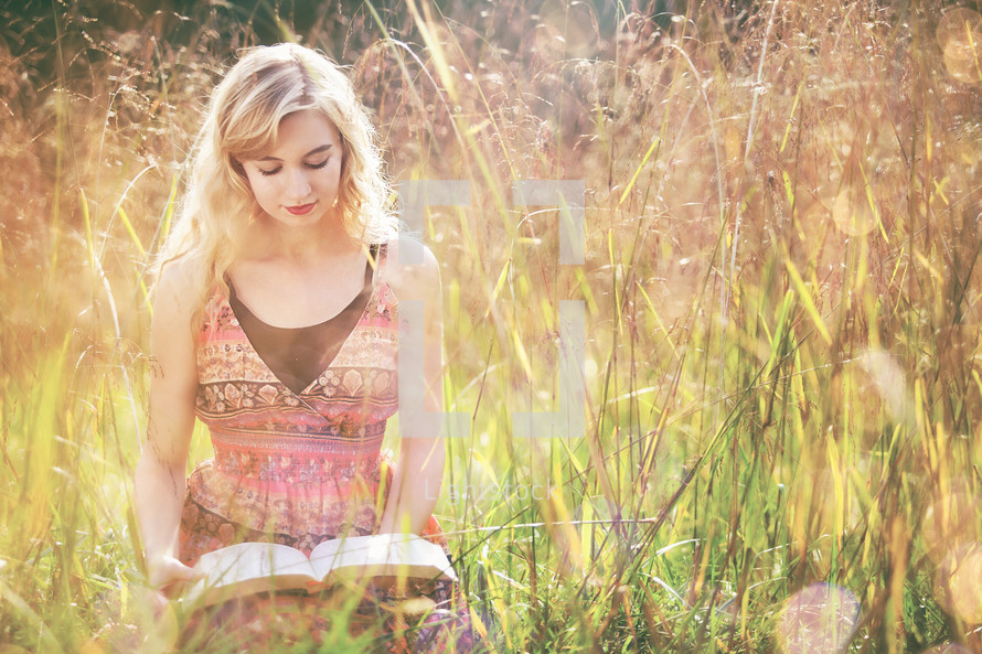 a woman sitting and reading a Bible in tall grass 