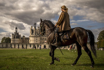 a woman riding a horse near a castle 