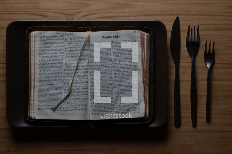 Table set with a plate, knife and two forks. On the plate, in stead of physical food there is spiritual food: The bible. The bible is an old translation into danish, revised to fit the norwegian language. It is printed in gothic script.