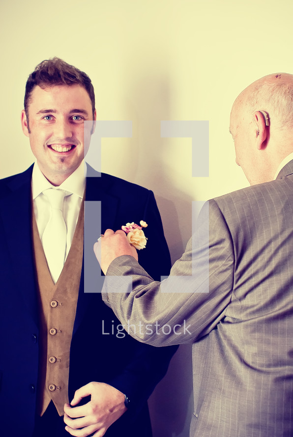 A father placing a boutonniere on his groom son. 