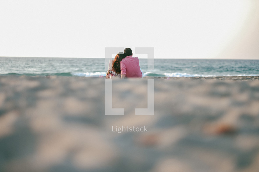 a couple snuggling sitting on a beach 