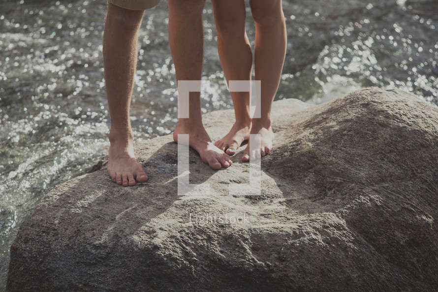 a couple standing on a rock with bare feet 