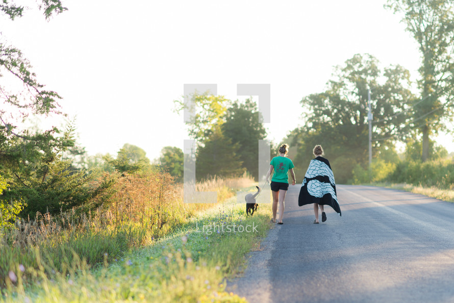 women walking down a country road walking a dog 