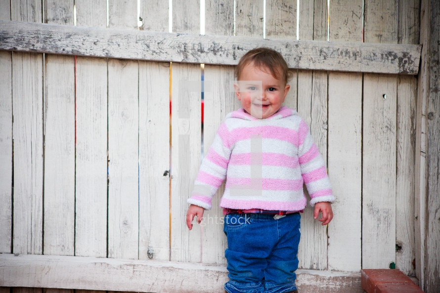 toddler girl against a white fence 