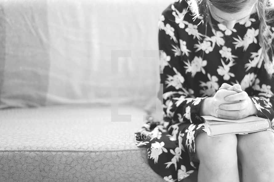 teen girl sitting on a couch praying over a Bible 