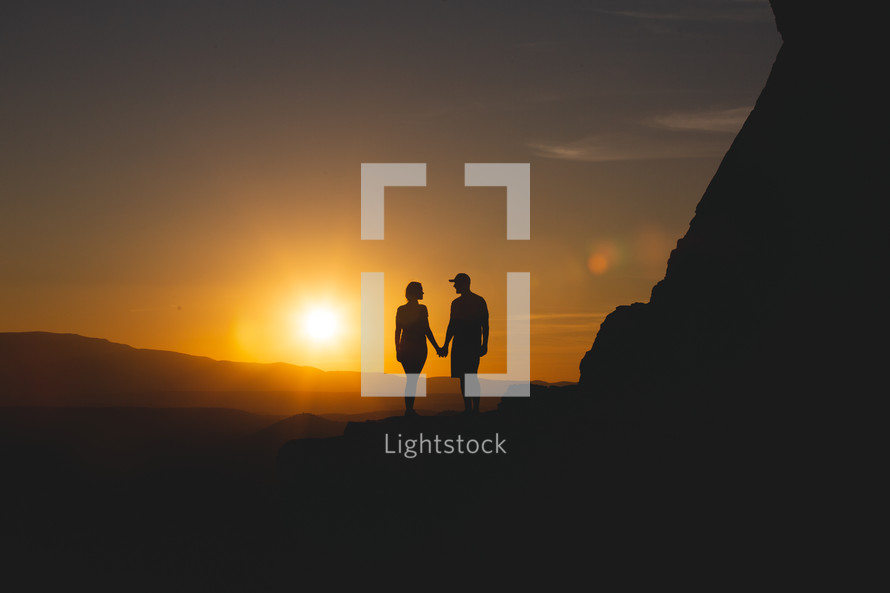 silhouette of a couple standing at the edge of a mountain at sunset 