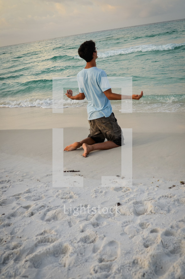 man kneeling in prayer on a beach 