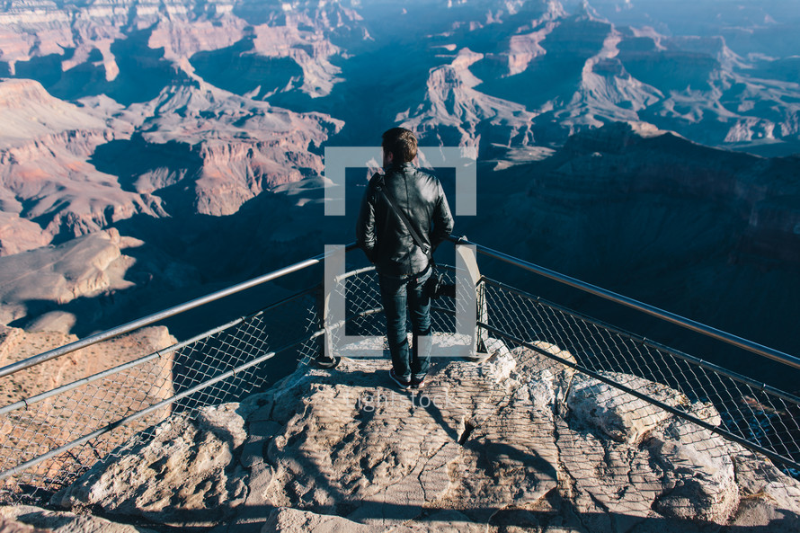 man looking out over a railing at a canyon below 