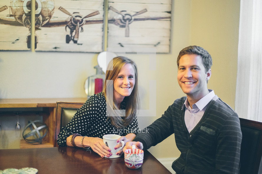 A smiling man and woman sitting at a table with coffee cups.