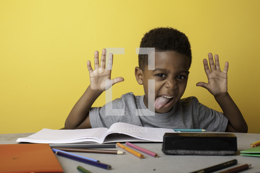 a boy child sticking his tongue out at his desk 