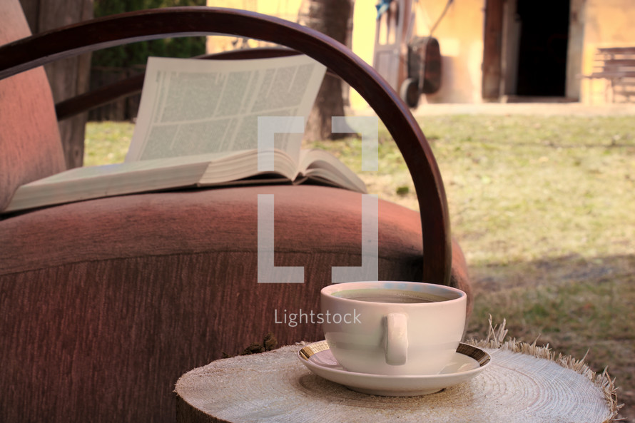 tea cup and open Bible in a chair outdoors 