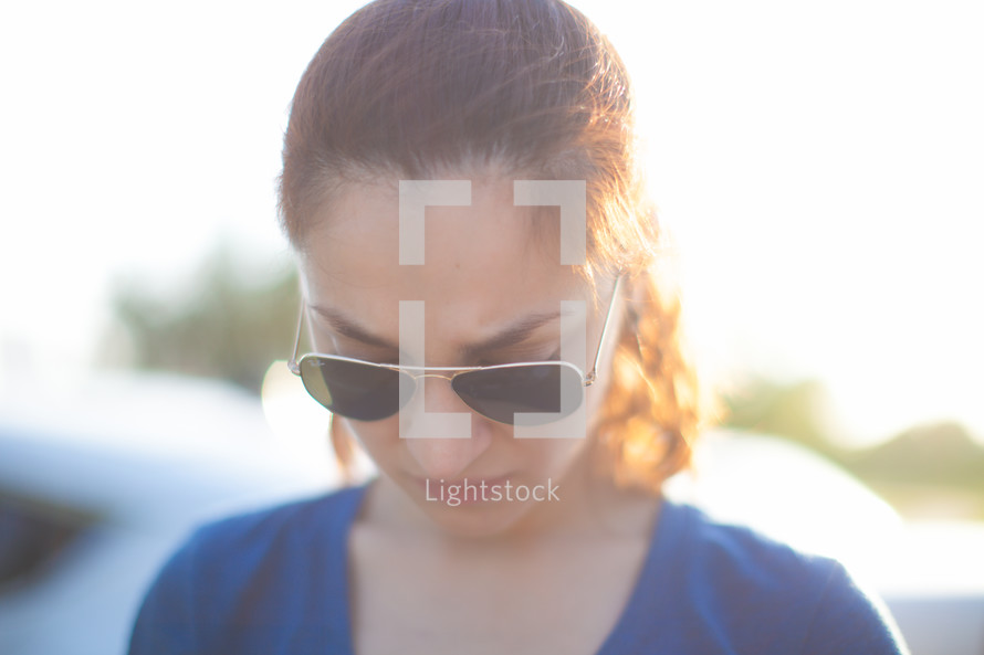 Woman in sunglasses praying outside.
