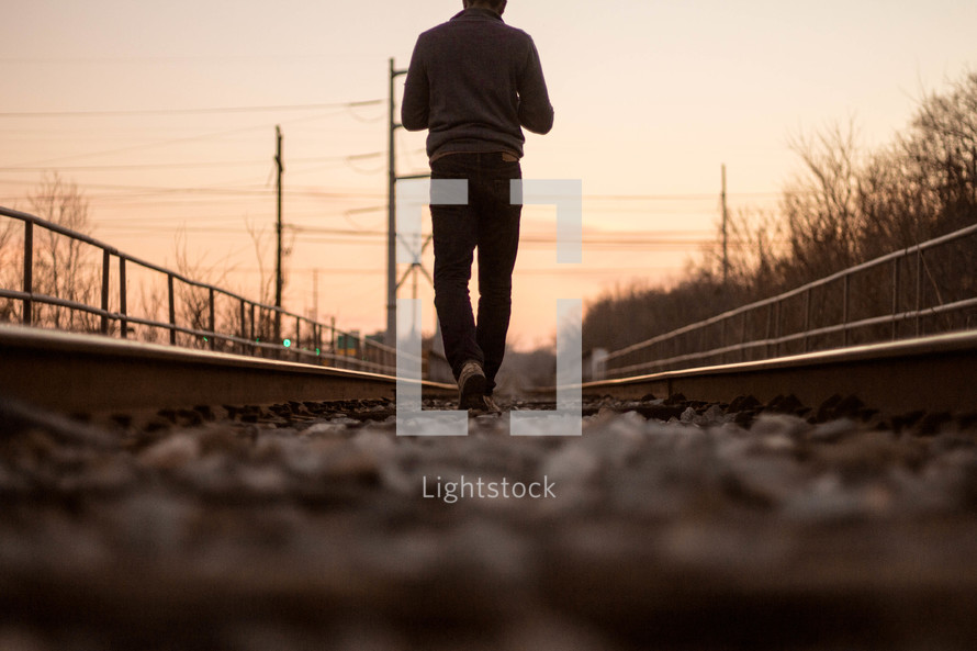 a man walking down tracks at sunset 