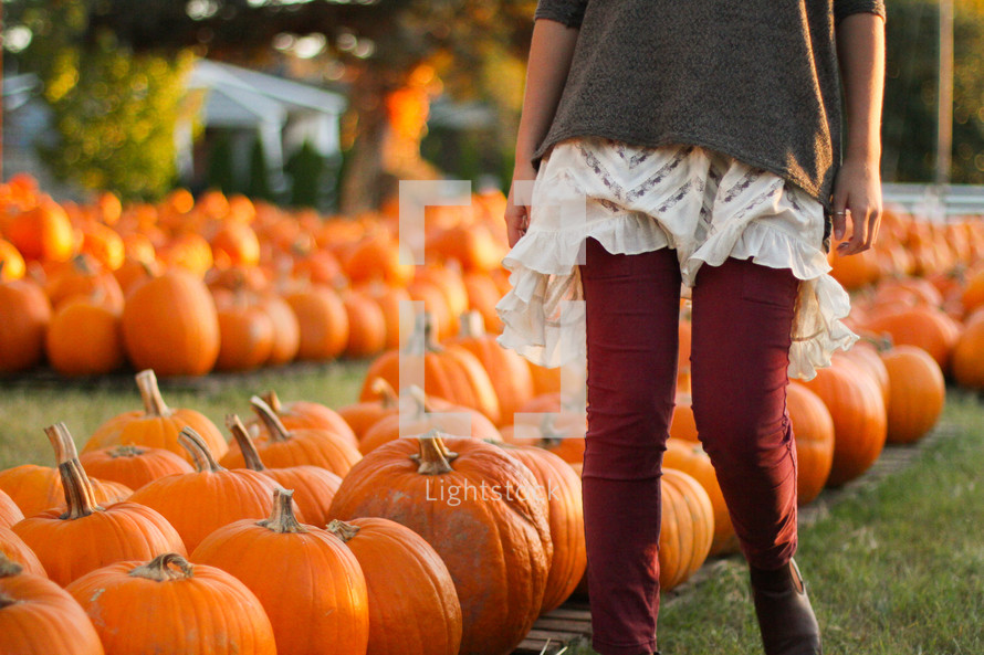 a woman walking through a pumpkin patch 