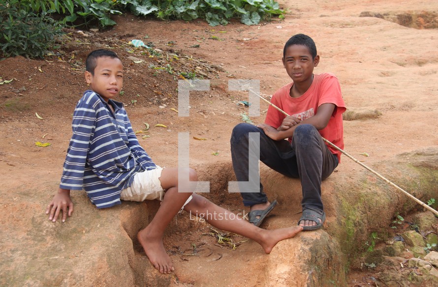 boys sitting on the ground holding a stick 
