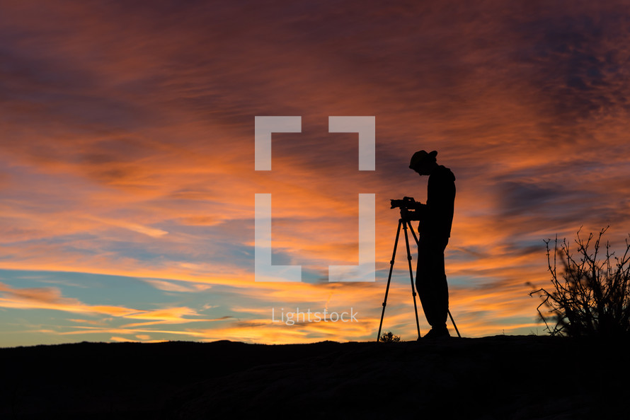 silhouette of a boy standing near a camera on a tripod at sunset 