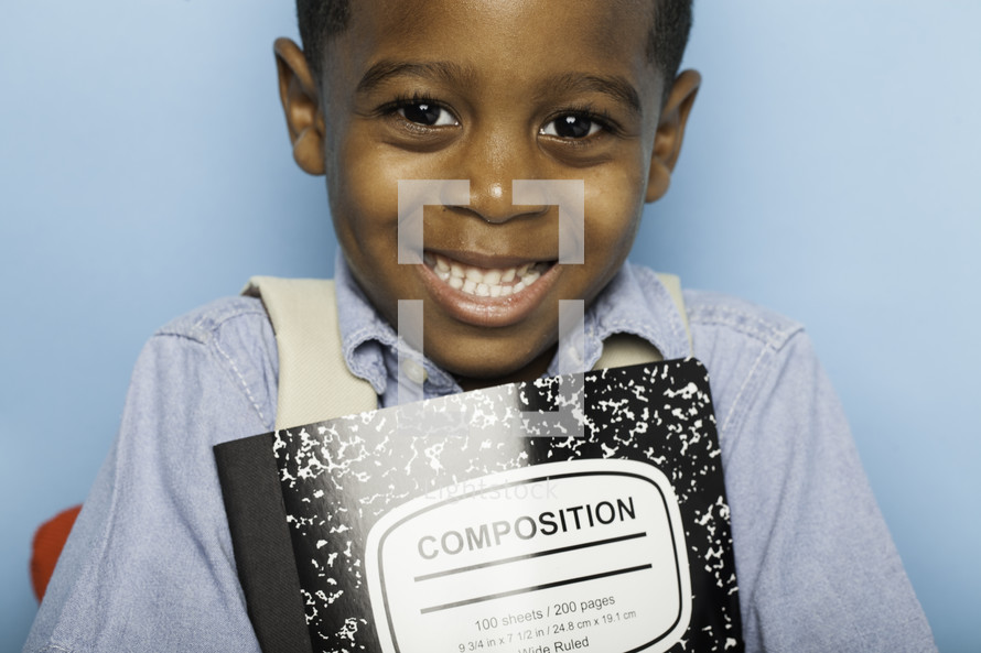 a smiling boy child holding a composition notebook 