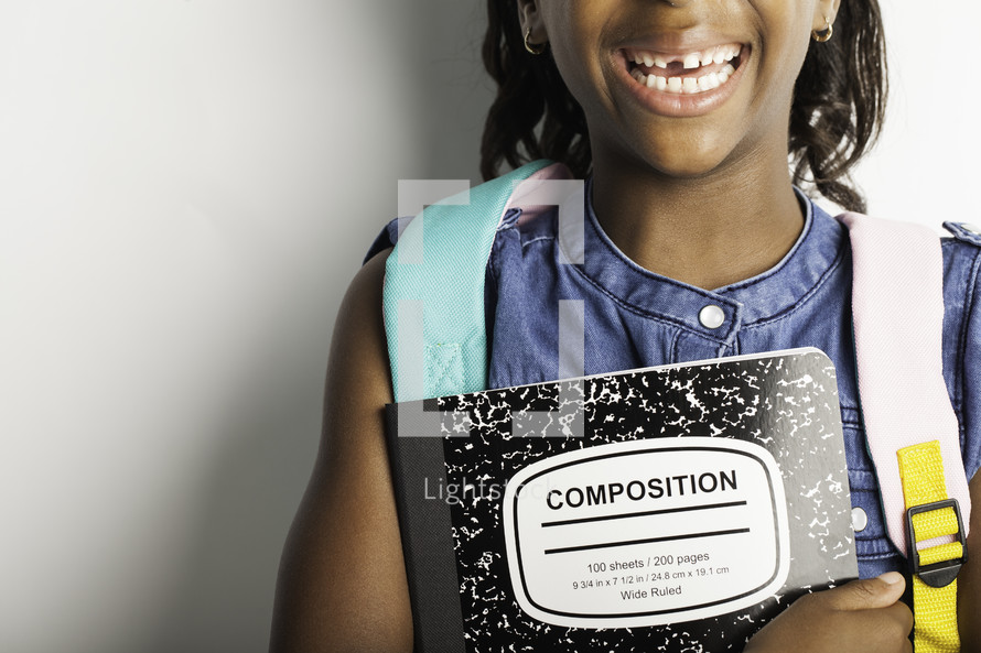 a smiling girl with missing teeth holding a composition notebook 