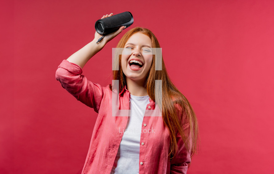 Woman dancing, enjoying on pink studio background. Girl moves to rhythm of music. Young teenager listening to music by wireless portable speaker - modern sound system. High quality