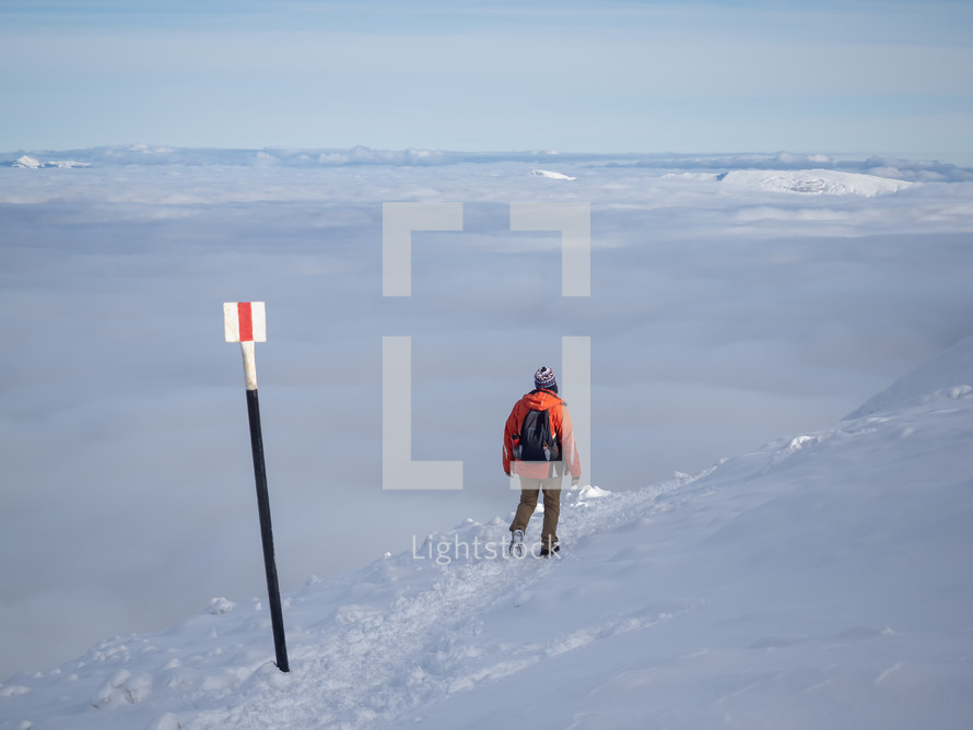 Man with backpack hiking on a mountain track above clouds in sunny day, Winter season with snow on mountain.