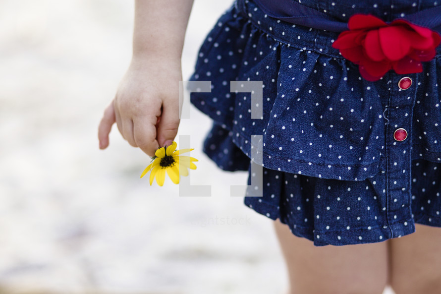 Lower portion of a small girl with a yellow flower in her hand.