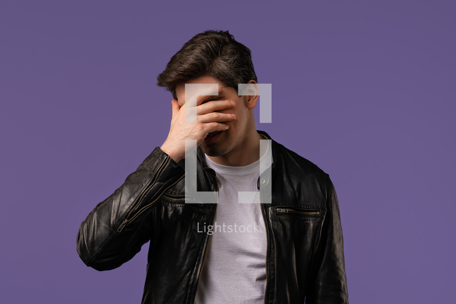 Worried man doing facepalm gesture, covering face with hands, like no, I forgot. Disappointed guy feeling sorrow, regret, drama, failure, problems on violet background. High quality