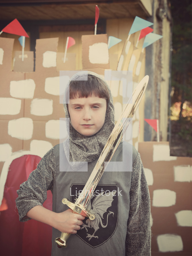 a boy holding a sword standing in front of a cardboard castle 