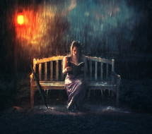 woman sitting on a bench reading a Bible in the rain 