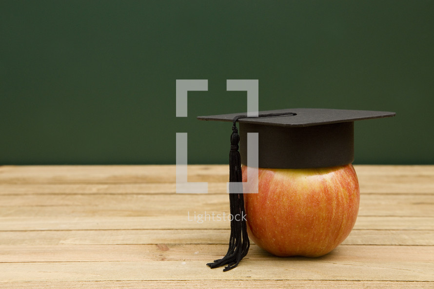 graduation cap on an apple on a desk