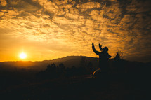 silhouette of a man with hands raised at sunset 