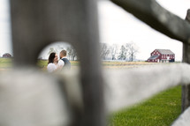 couple hugging outdoors through a hole in a fence post 