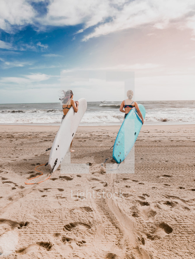 two women on the beach with surfboards 