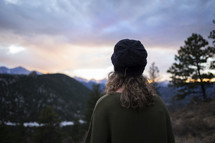 a woman in a wool cap standing on a mountaintop at sunrise 